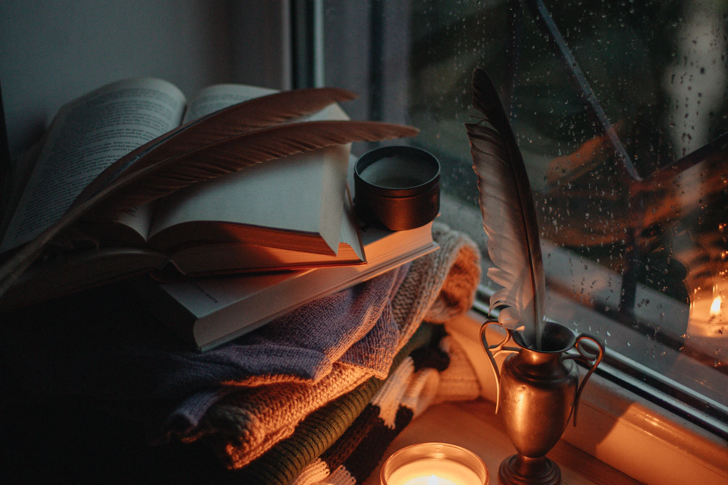 A stack of thrillers with a quill and a candle by a rainy window, the right mood for books like Verity