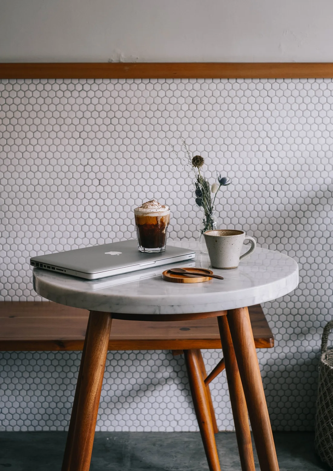 A laptop, iced coffee, and ceramic mug on a marble cafe table