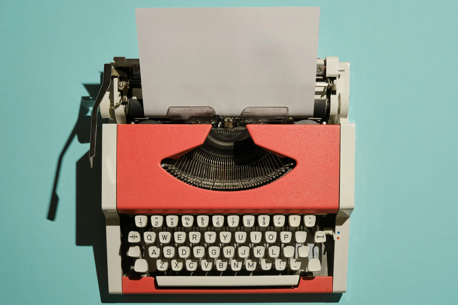 A red vintage typewriter with a blank page on a bright turquoise background