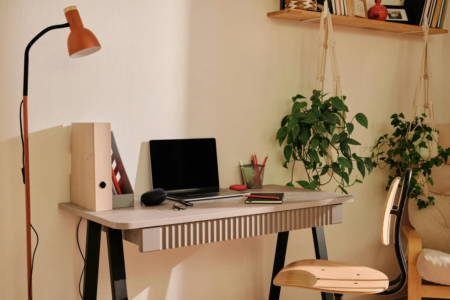 A cozy writing desk with a laptop, lamp, and hanging plants