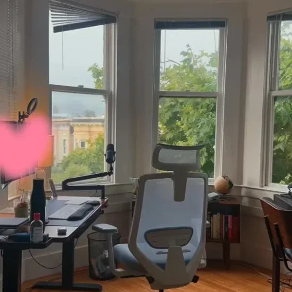 A standing desk and blue chair in a bay window with San Francisco rooftops and trees outside