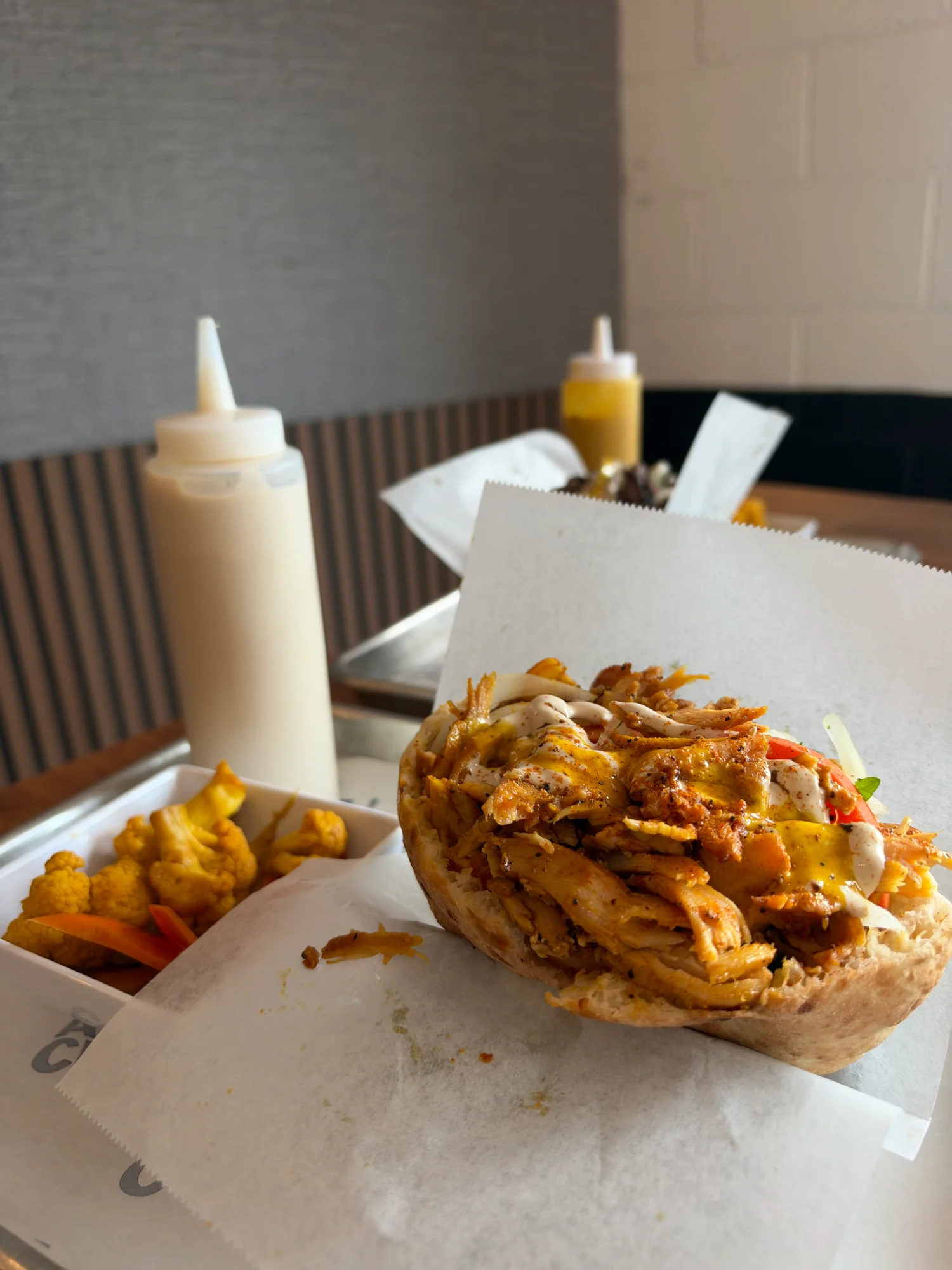 The chicken shawarma half pita with tahini and amba at Avi Cue in Studio City, Los Angeles, next to a dish of bright yellow pickled cauliflower