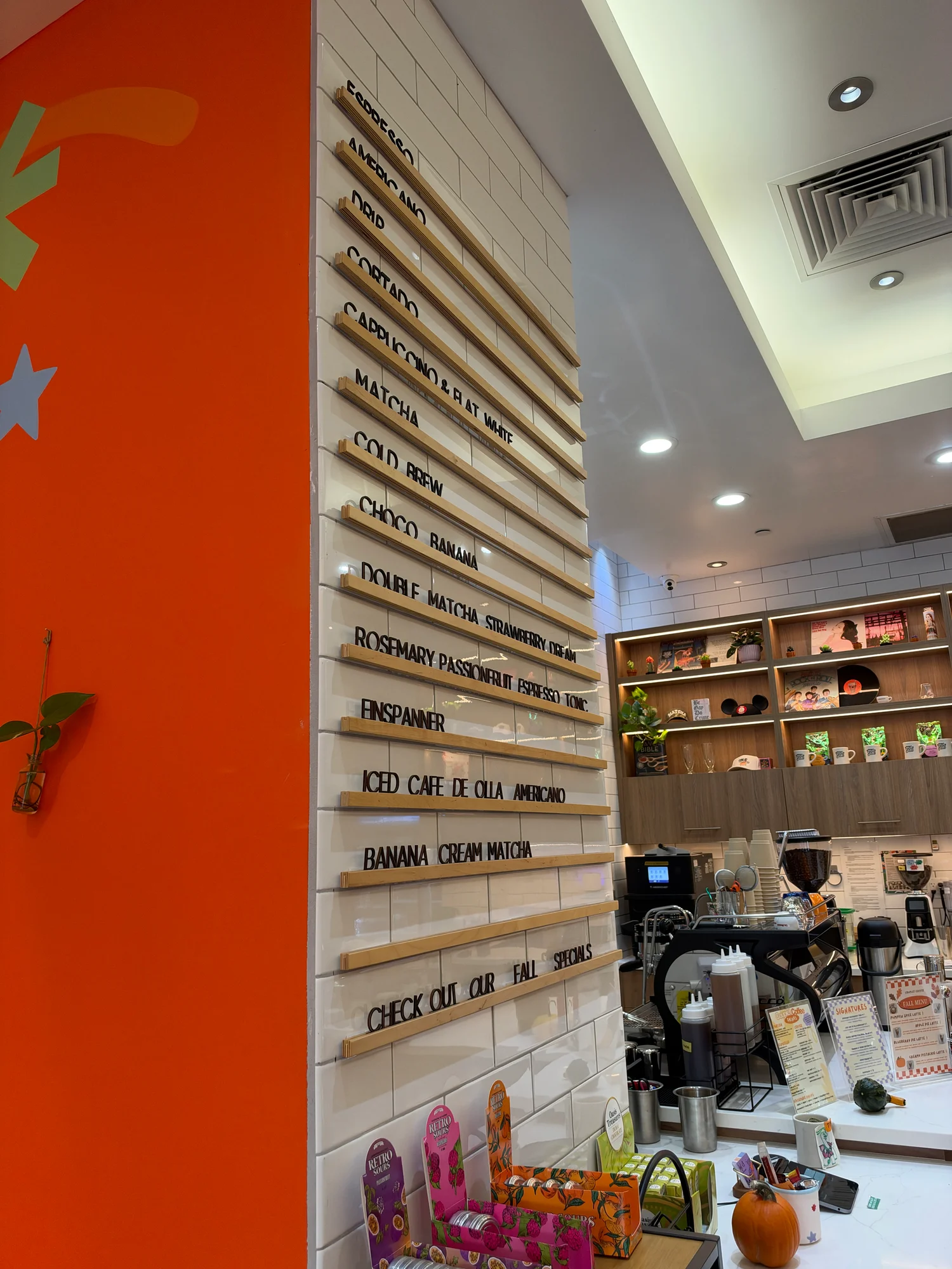 The menu board at Couplet Coffee Hollywood, with drinks from espresso and cortado down to the Banana Cream Matcha, next to the espresso bar and a small pumpkin on the counter