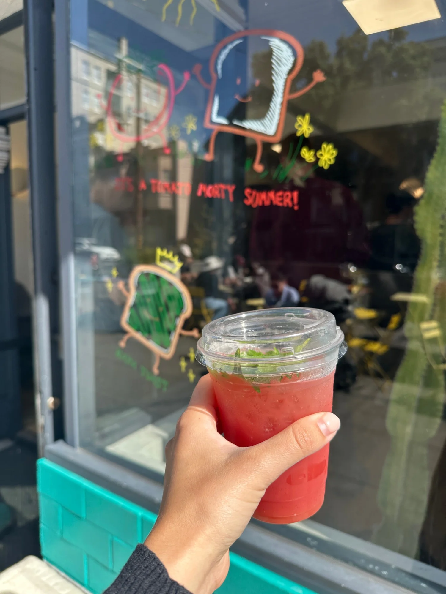 Watermelon lychee iced tea in front of the illustrated storefront window at Breadbelly San Francisco