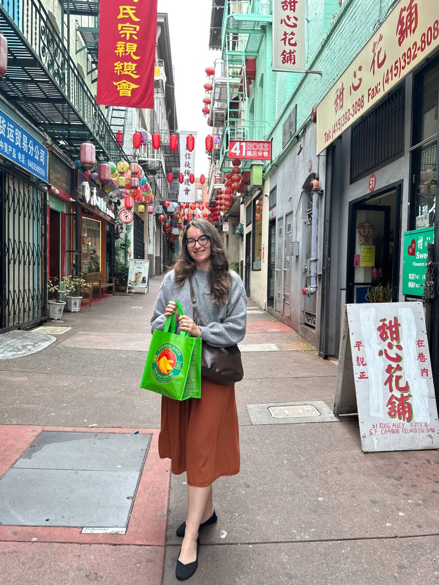 Amy holding a Golden Gate Fortune Cookie Factory bag under the lanterns of Ross Alley