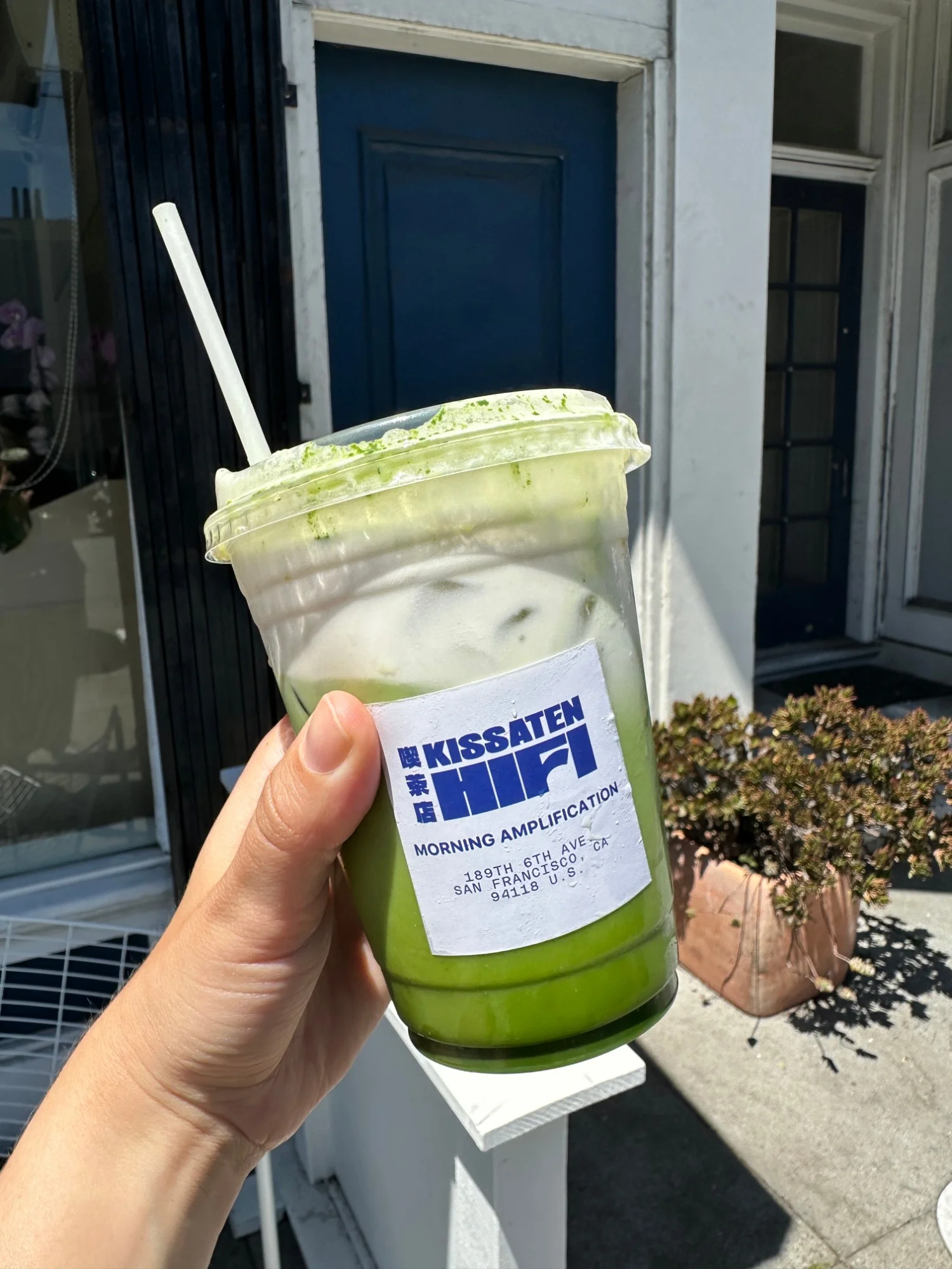 An iced matcha latte from Kissaten Hi-Fi held up outside the shop on 6th Ave in San Francisco