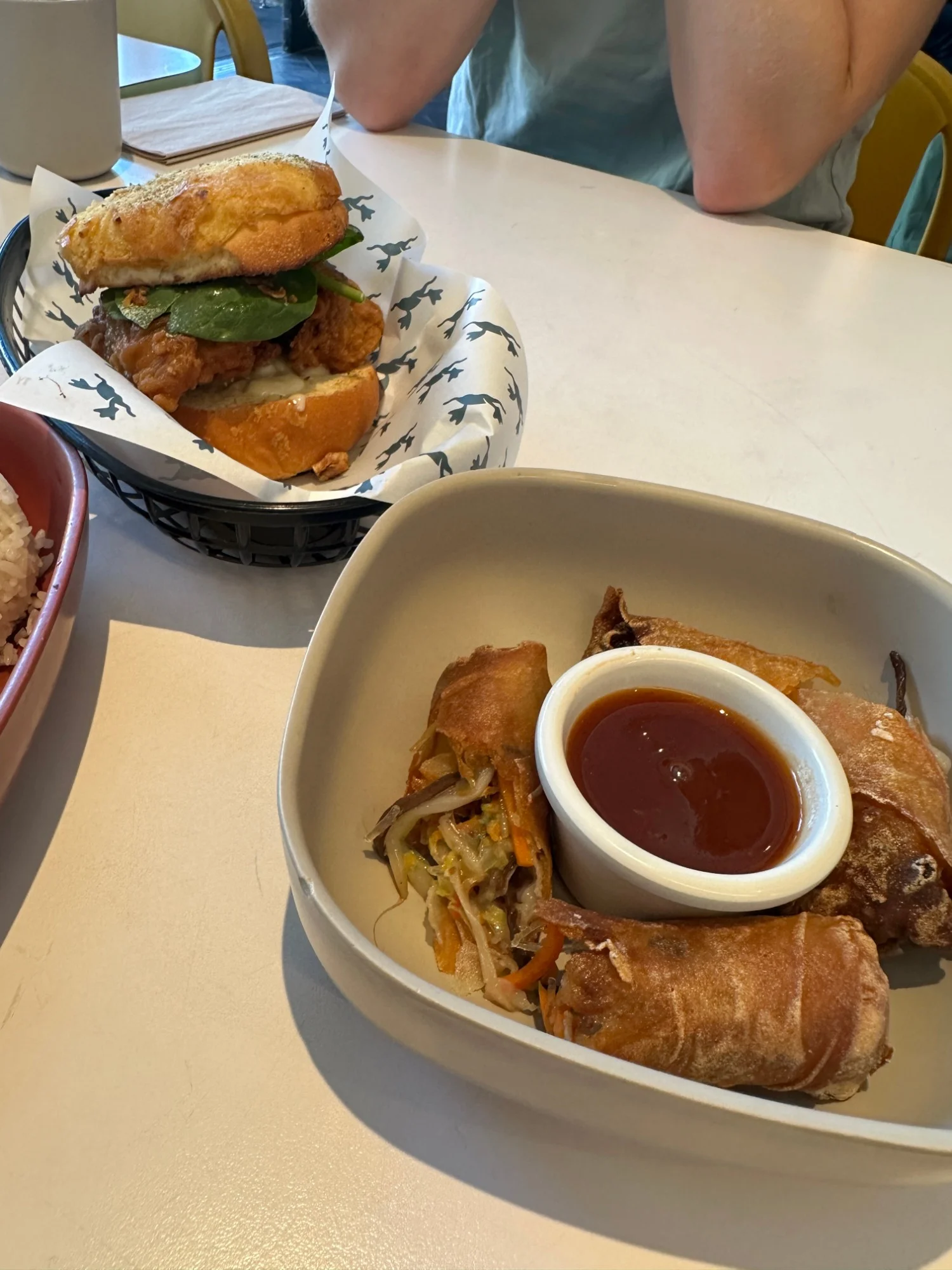 Mamahuhu’s egg rolls with sweet and sour dipping sauce, with the Super Savory pineapple bun chicken sandwich behind them