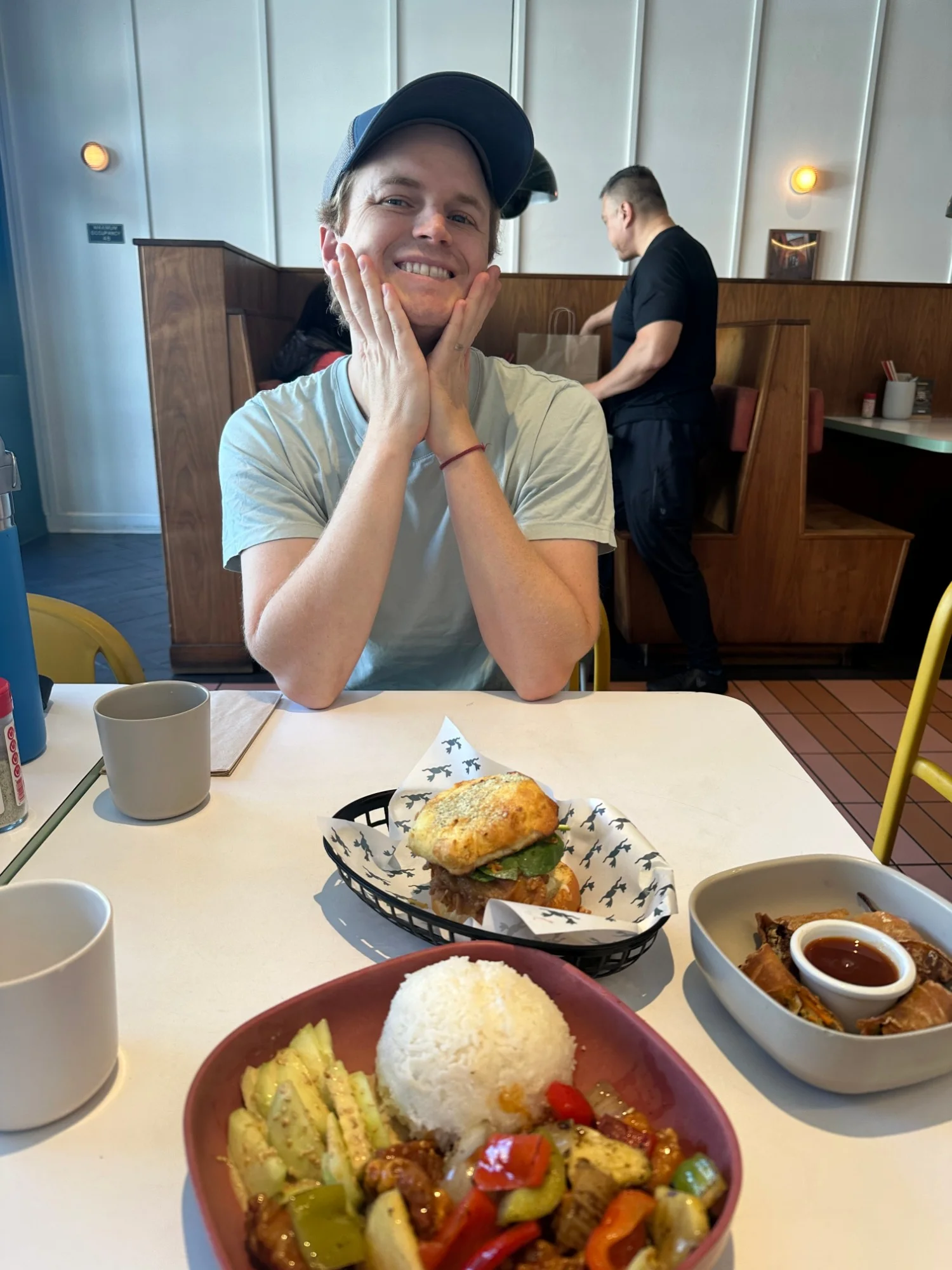 Kyle at a table at Mamahuhu in San Francisco with the Super Savory sandwich, the egg rolls and the sweet and sour chicken rice plate