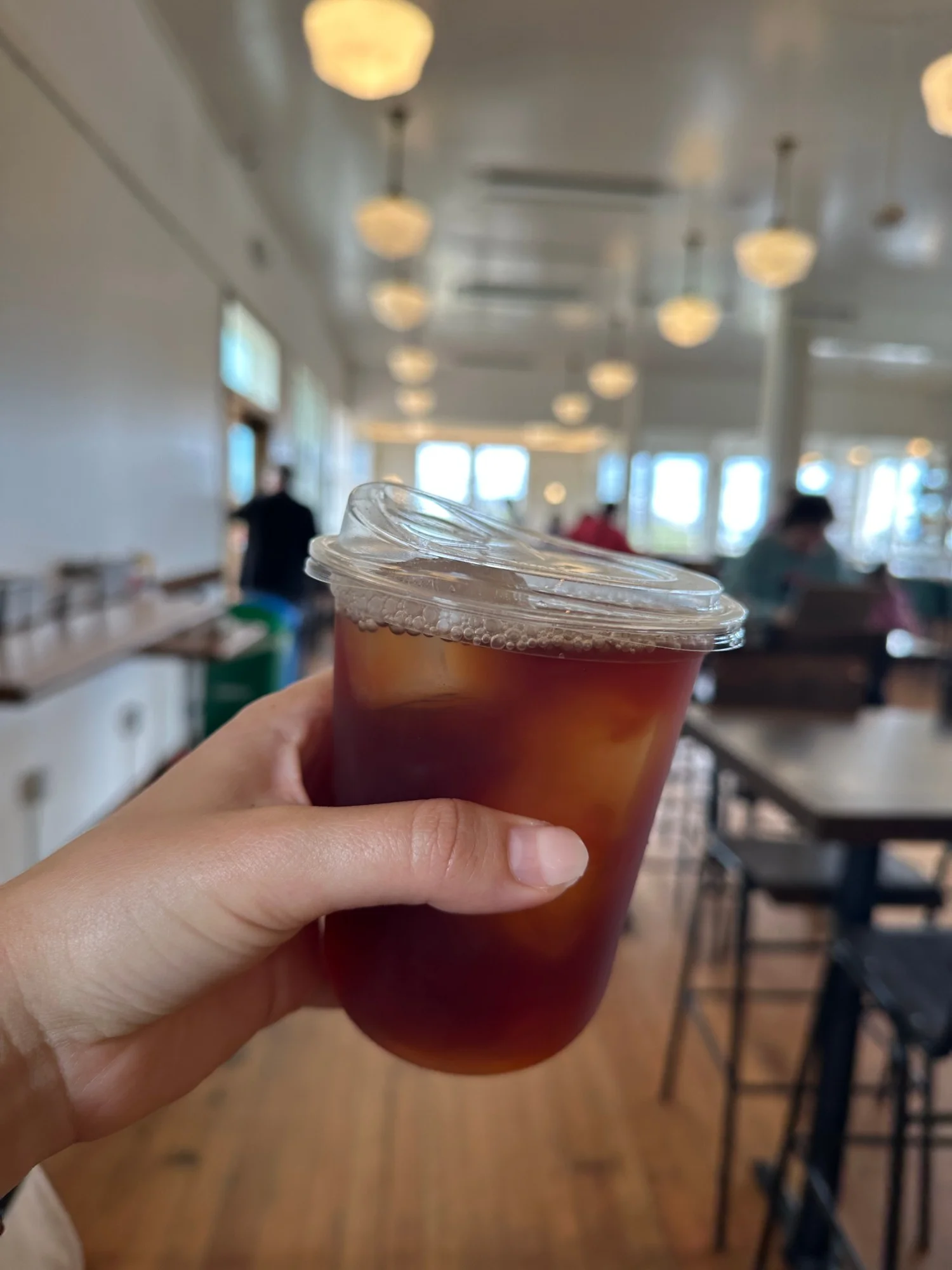 An iced tea inside the Mess Hall at the Presidio in San Francisco, with the food hall's pendant lights and windows behind it