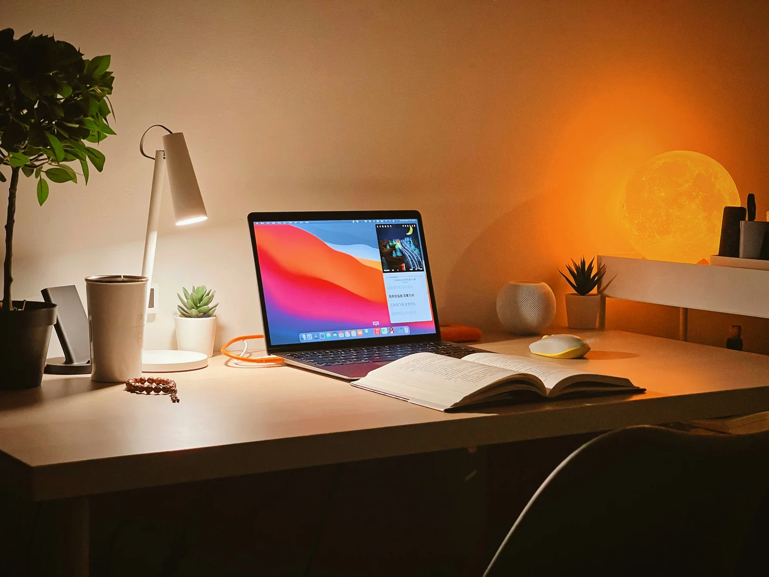 A laptop and open notebook on a desk in warm evening lamplight