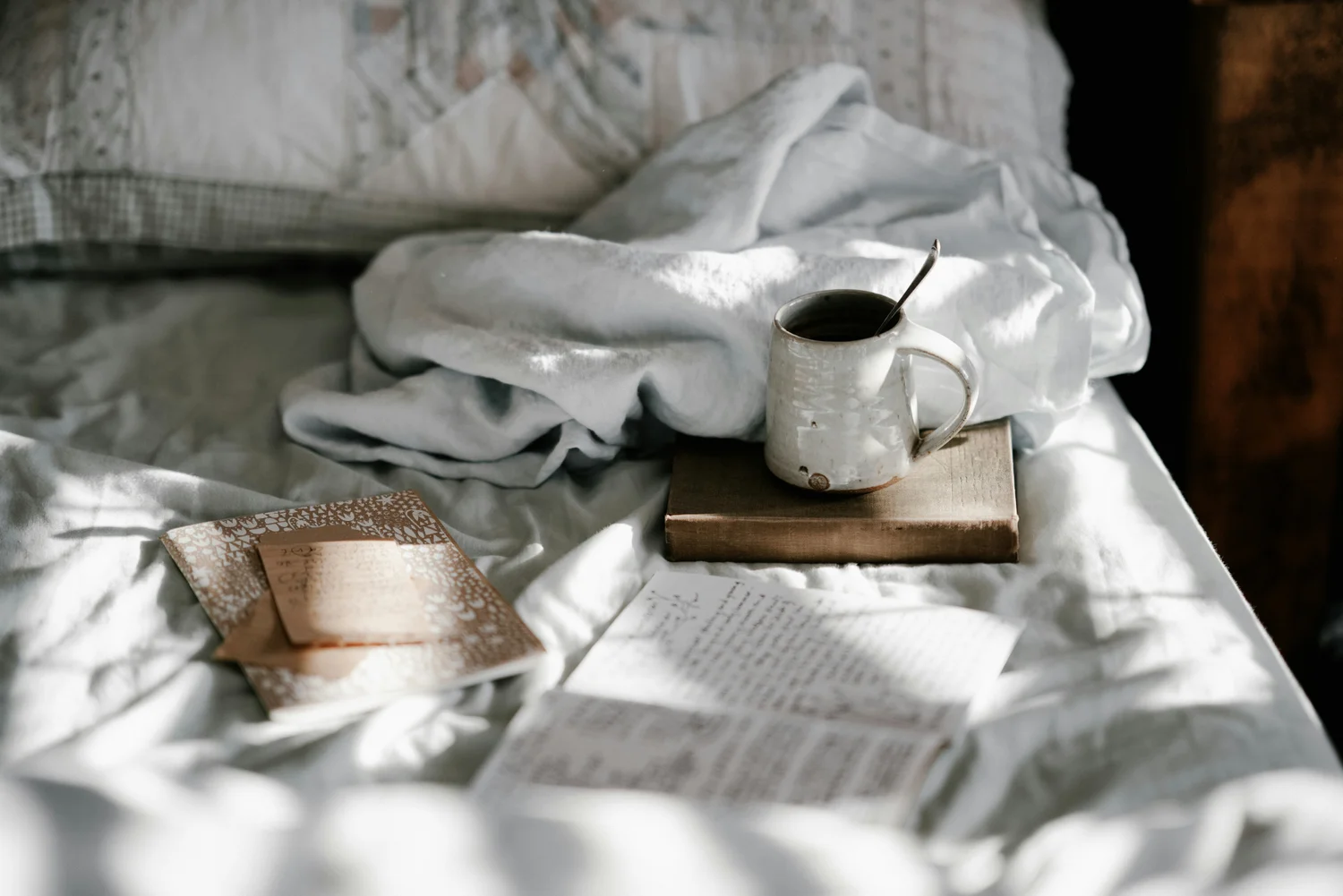 A mug of coffee on a book in bright morning bedding with handwritten notes