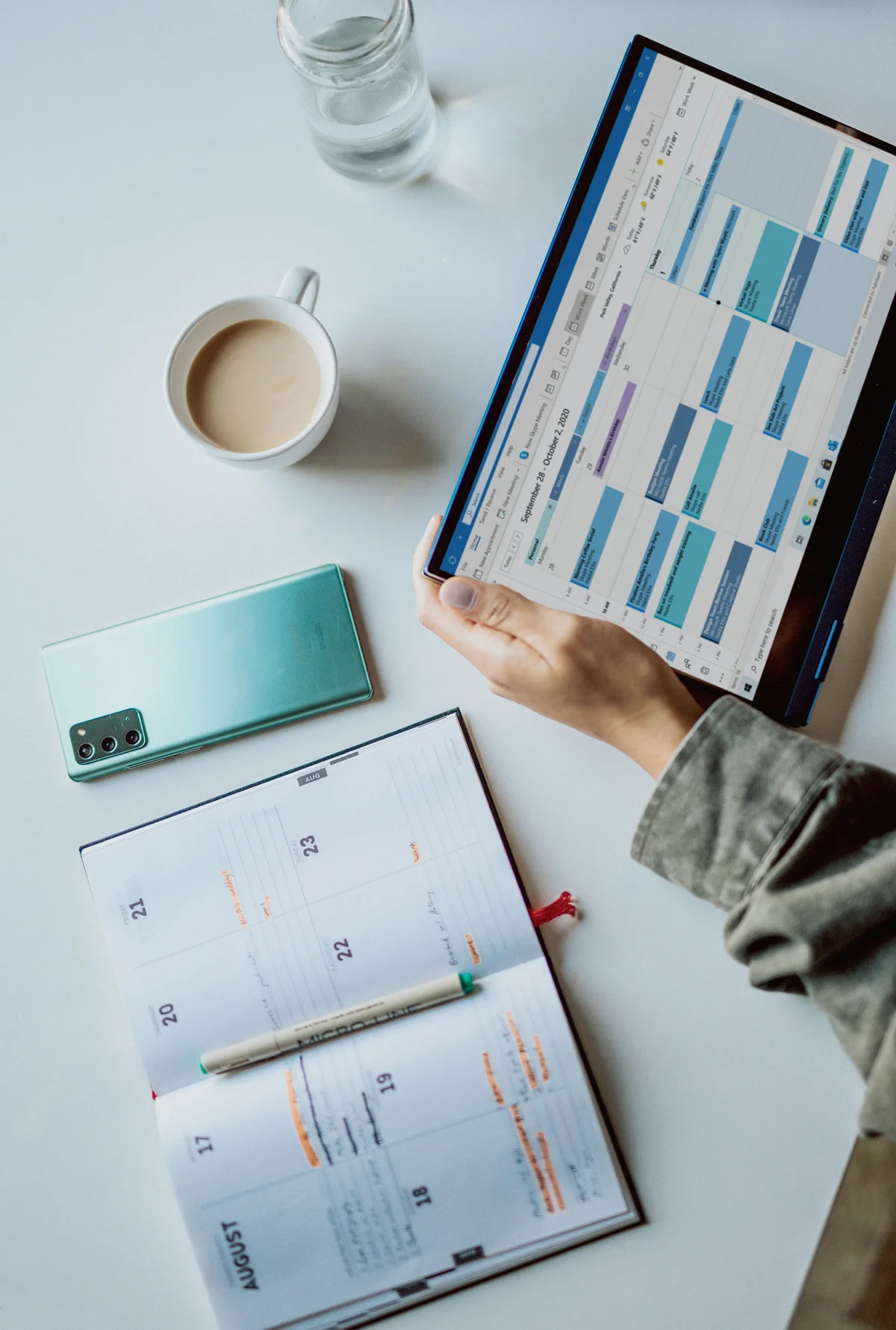 A planner, tablet calendar, and coffee on a white desk