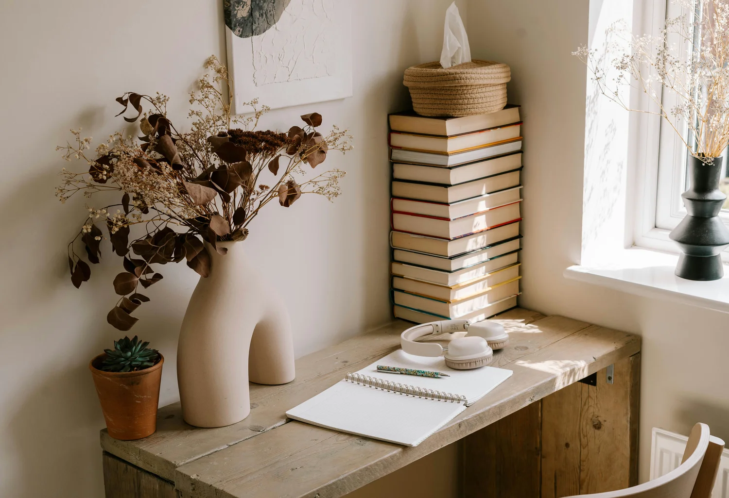A stack of books on a rustic desk by a bright window