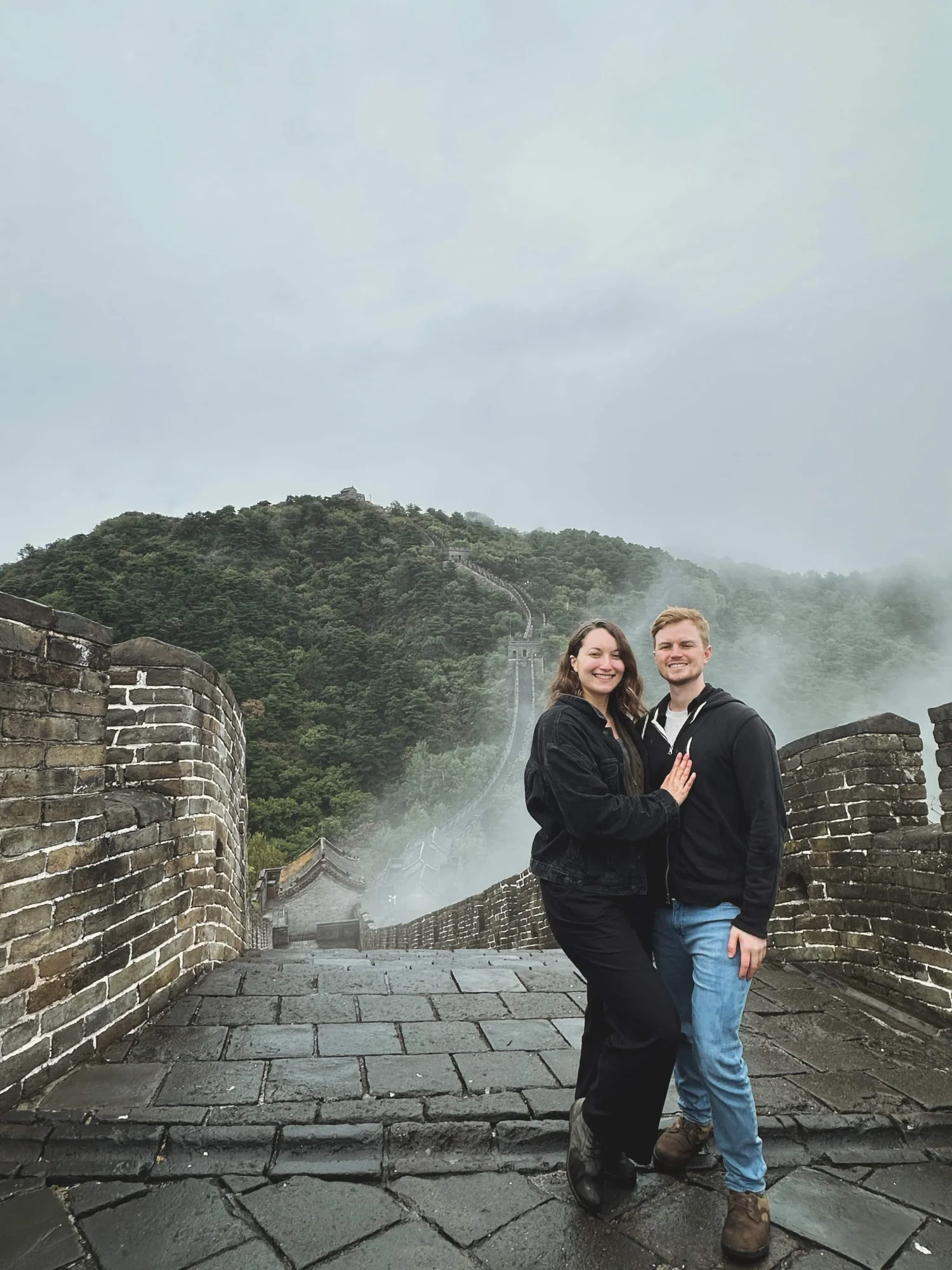 Couple on the Great Wall of China during a guided Great Wall of China tour from Beijing. Rain-cleared skies, mountain views, and ancient stone steps create the perfect moment from their Great Wall of China trip.