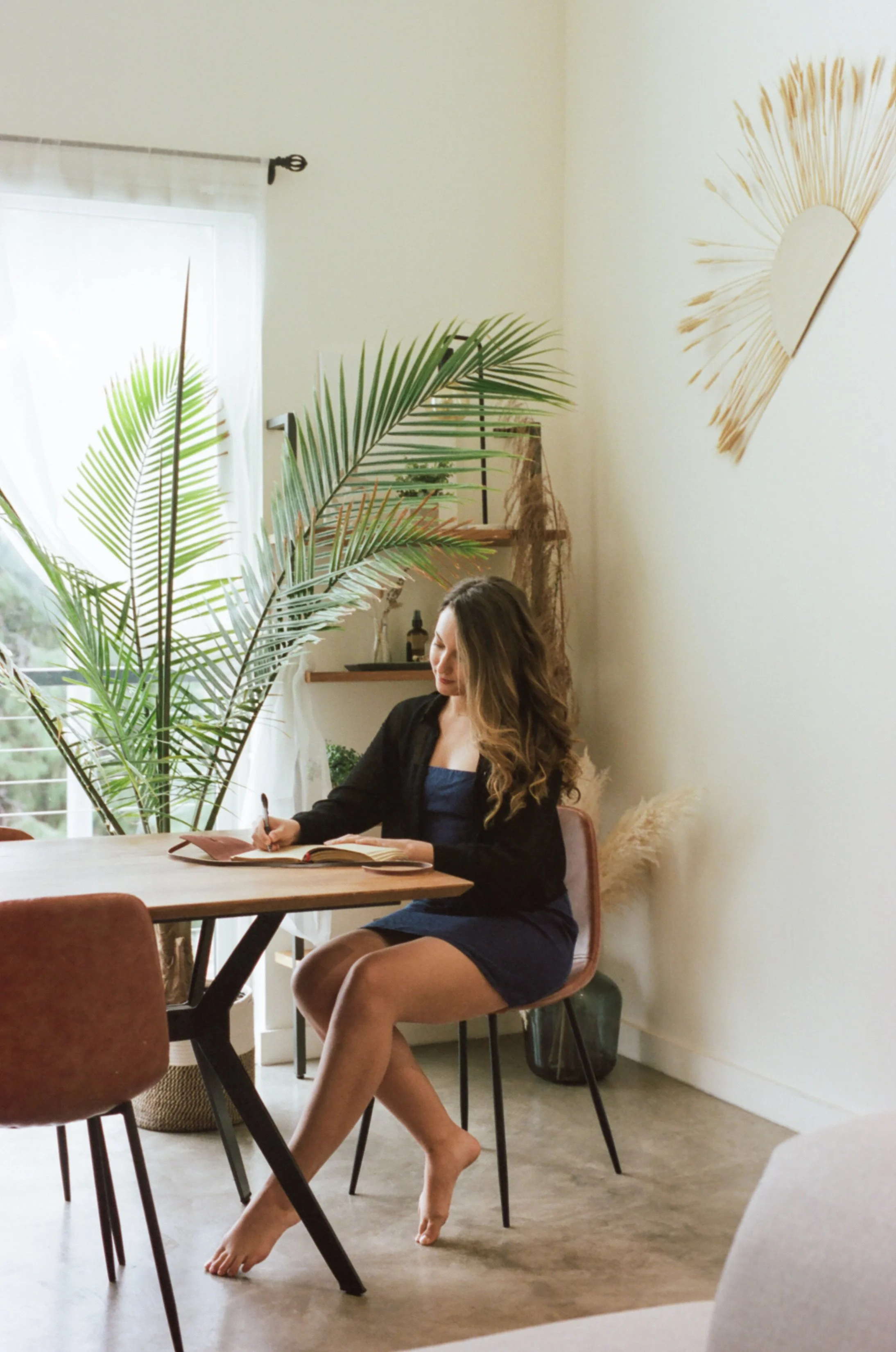 Amy Suto writing in a journal at a serene, plant-filled workspace, reflecting her memoir ghostwriting and creative storytelling expertise.