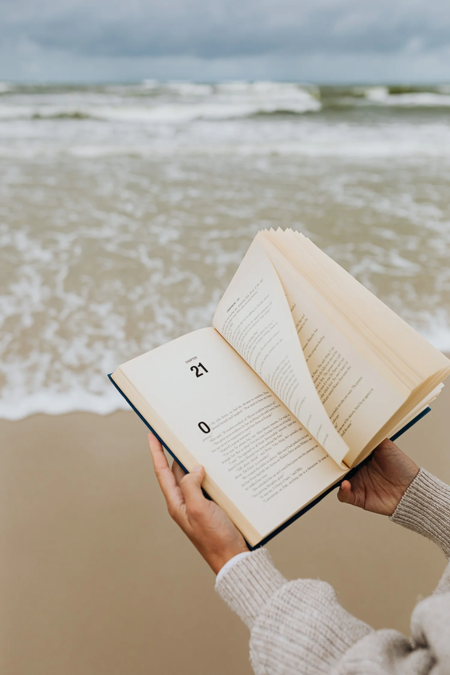 Hands holding an open book by the ocean, representing the transformative power of developmental editing with Amy Suto to bring clarity and depth to your manuscript.