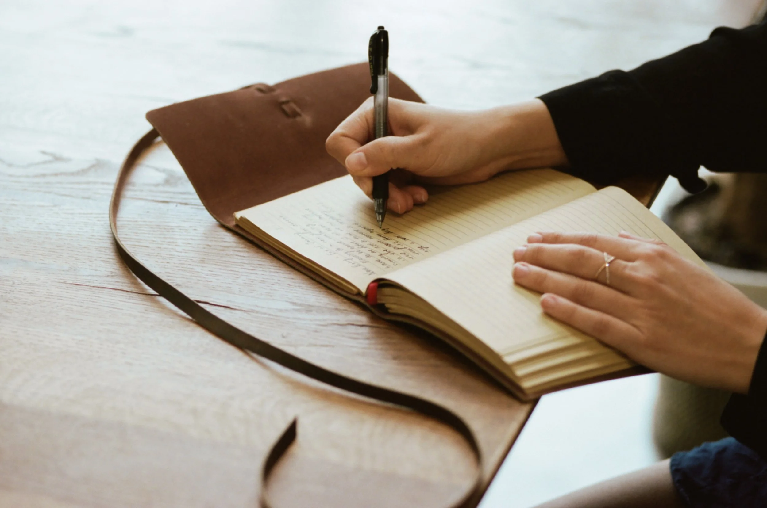 Hands writing in a leather bound notebook