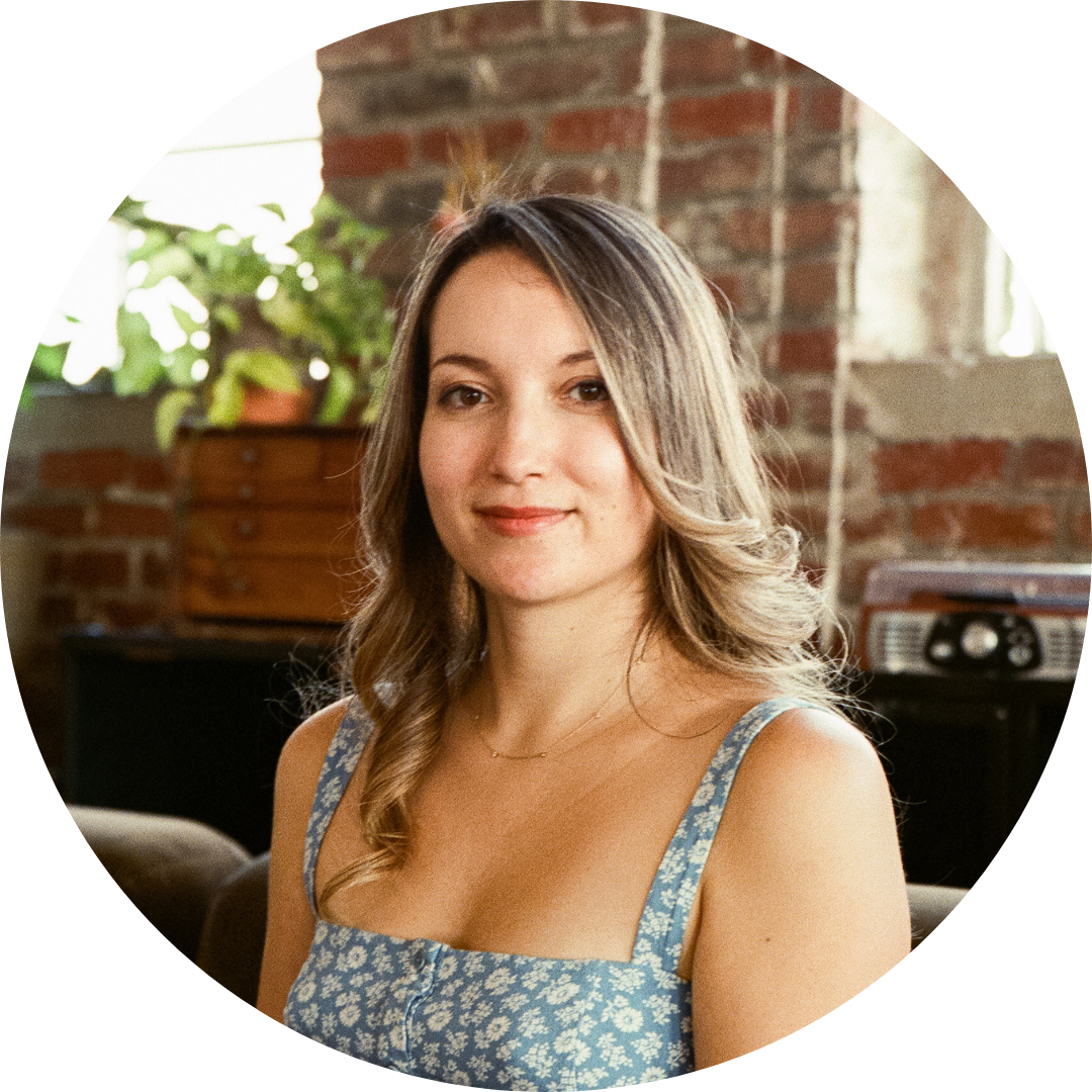 Amy Suto, memoir ghostwriter and founder of the Writing Job Board, seated in a cozy, creative workspace with a brick wall and plants in the background.