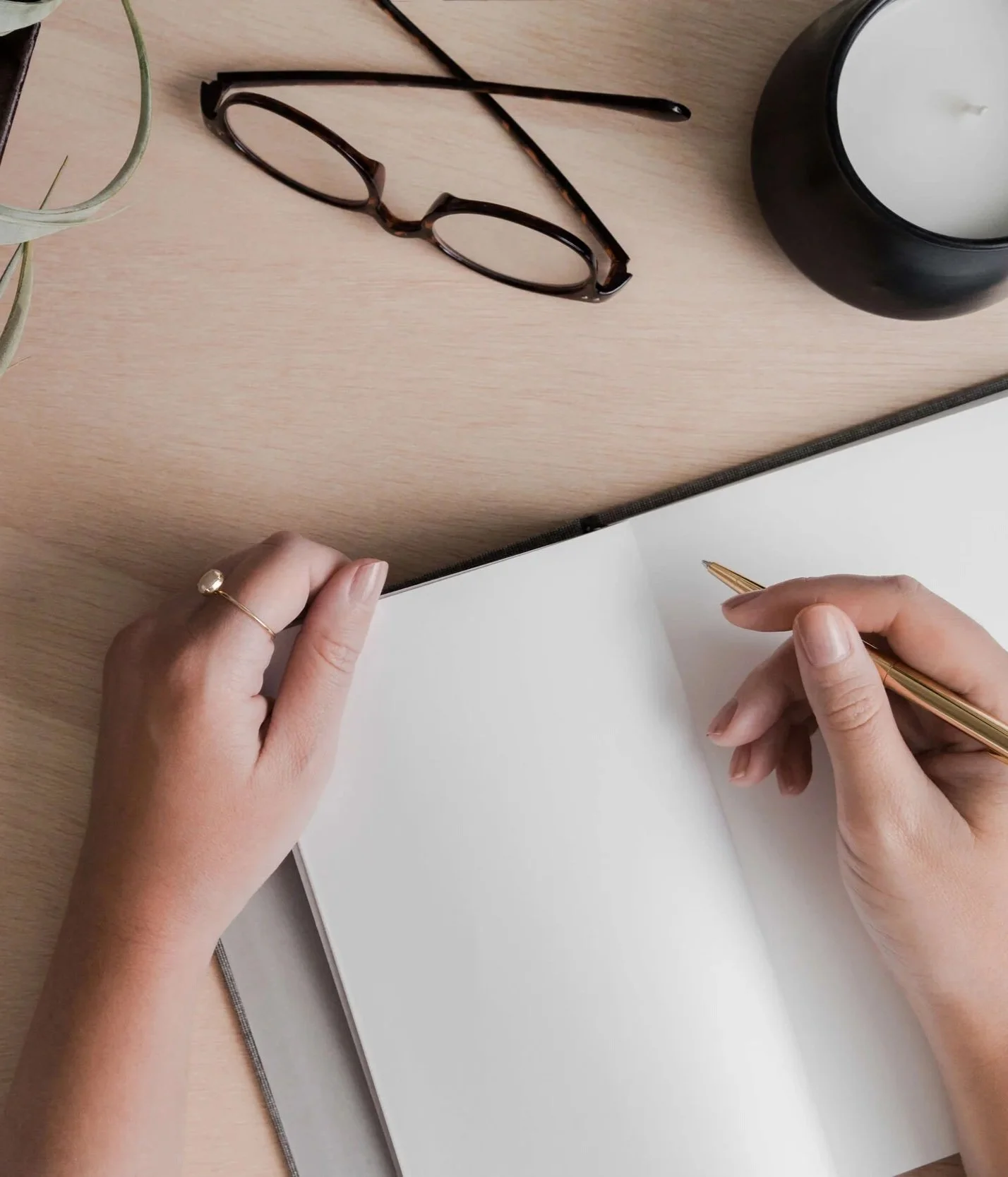 hands writing in a blank note book on a neutral desk